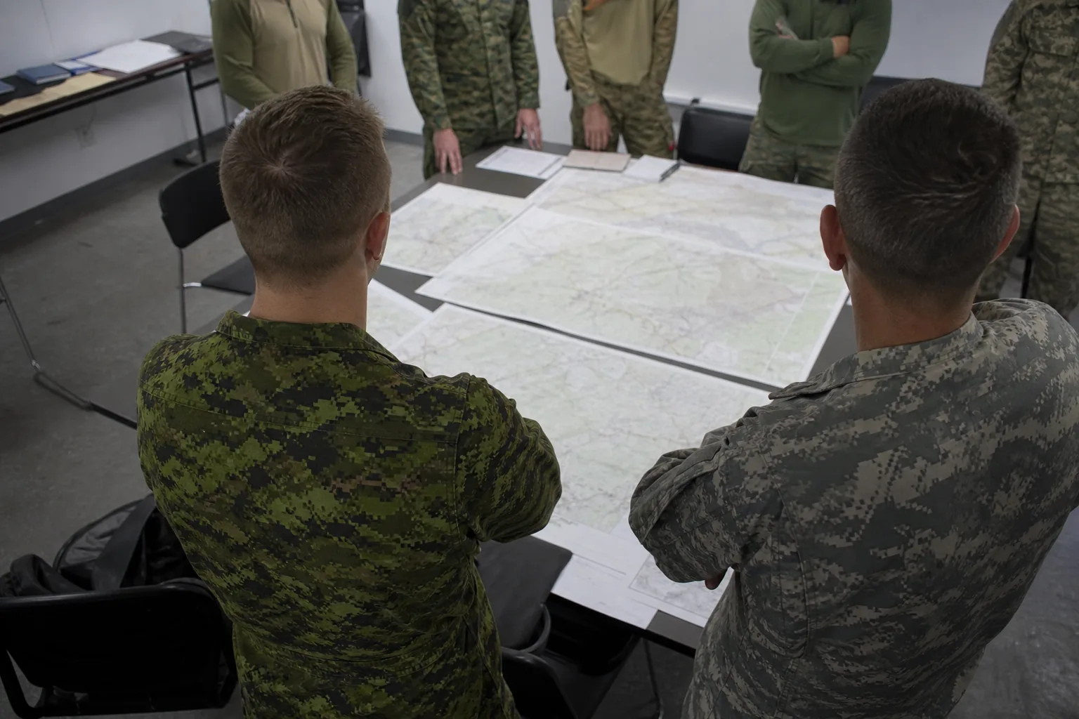 Officers in uniform standing around a table covered with paper maps in a plain briefing room (AI-generated image)