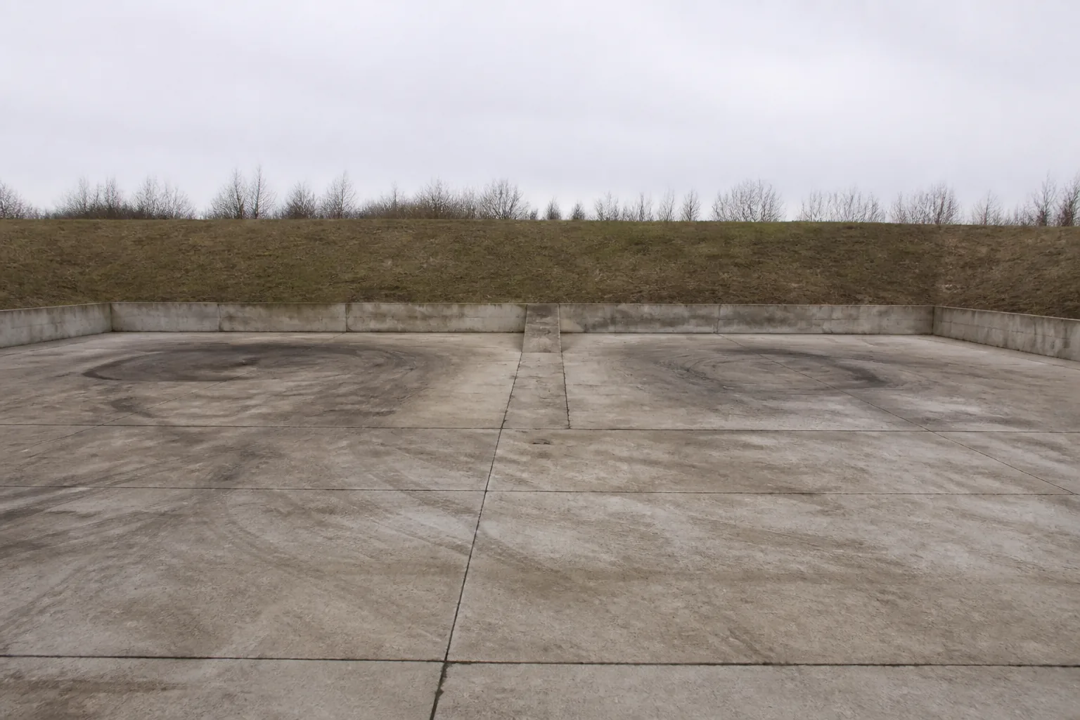 Two empty tank hardstands side by side on a concrete pad, oil stains and track scuffs on each (AI-generated image)