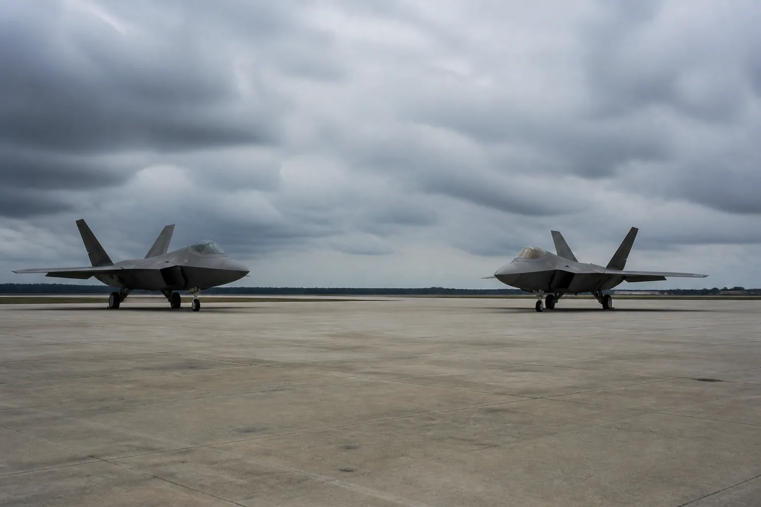 Two grey stealth fighter aircraft parked apart on a wide concrete apron under heavy overcast (AI-generated image)