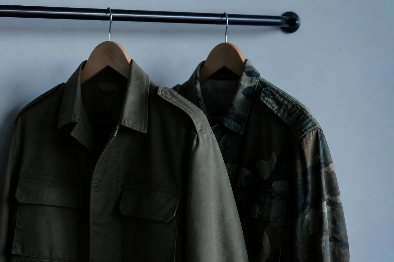 Two uniform jackets hanging side by side on a rail against a plain wall in cool window light (AI-generated image)