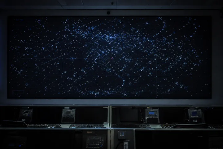 A debris-tracking wall display in a dim operations room, the screen dense with small marks and the consoles below unmanned (AI-generated image)