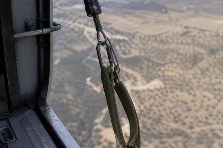 A hoist cable and rescue strop hanging from an open helicopter door, the ground far below out of focus (AI-generated image)