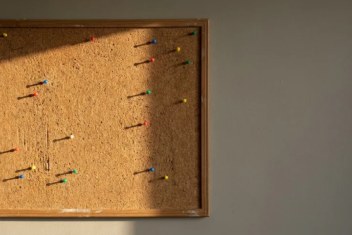 A wooden-framed cork board with scattered colourful pushpins (AI-generated image)