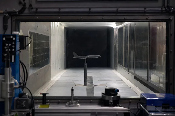 A wind-tunnel test section seen through thick observation glass, a small model on a sting mount inside (AI-generated image)