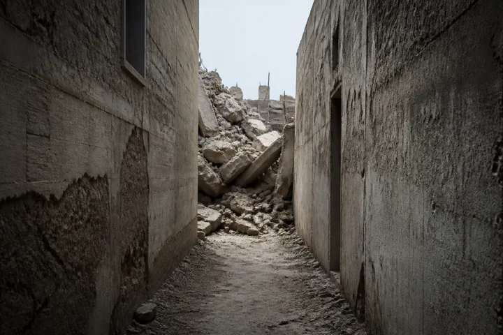 A narrow alley between concrete walls with rubble at one end and a strip of hard sky above (AI-generated image)