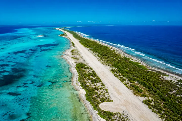 A coral runway strip on a low atoll seen from the air, lagoon on one side and reef on the other (AI-generated image)