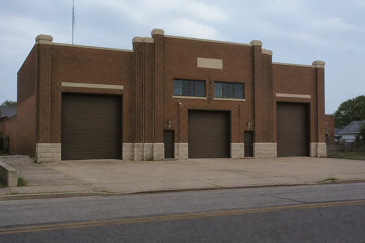 A small-town armory on an ordinary street: brick facade, roller doors and an empty parking apron (AI-generated image)