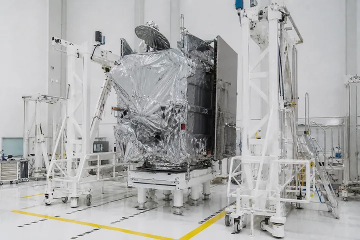 A clean-room bay with a satellite bus wrapped in protective film under bright even light, gantries around it (AI-generated image)