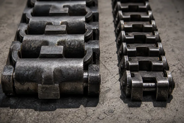 Two different tank track link designs lying side by side on a concrete floor, one wider (AI-generated image)