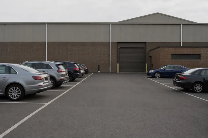 A half-full car park at an armory on a weekend morning, painted bays and a roller door beyond (AI-generated image)