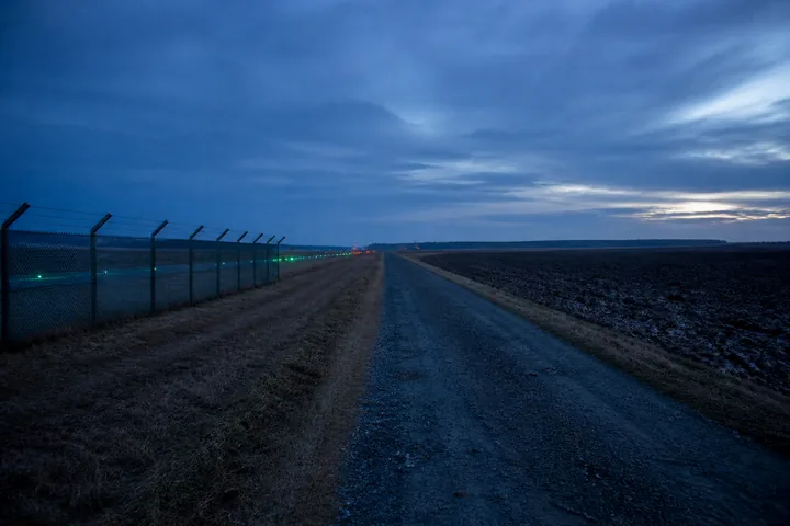 An airfield perimeter road with taxiway lights on one side and a ploughed field on the other (AI-generated image)