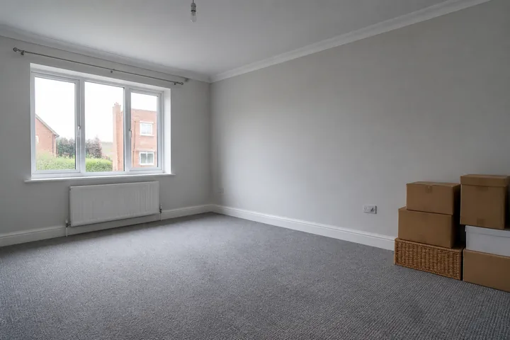 An empty living room with bare walls, a single curtain rail and boxes stacked in one corner (AI-generated image)