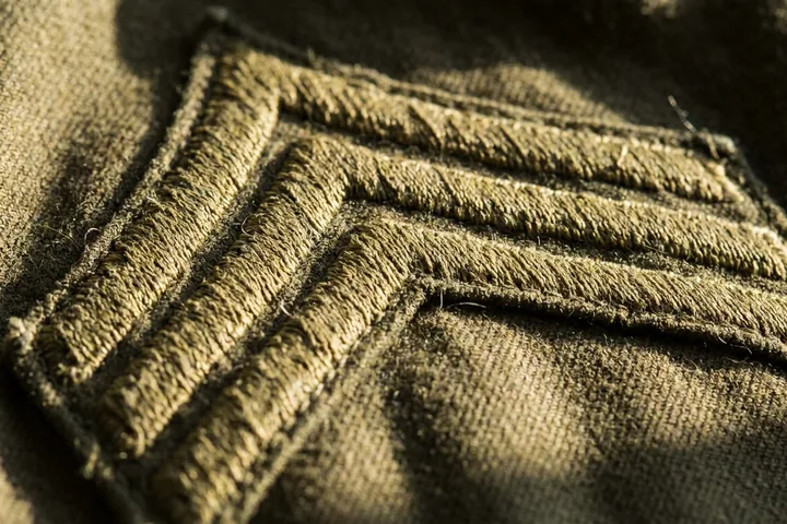 Three stacked, olive green embroidered chevrons on textured matching fabric (AI-generated image)