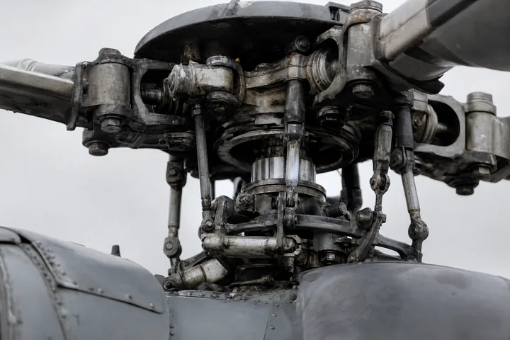 A close view of a helicopter rotor head and swashplate assembly, grease and wear visible on the linkages (AI-generated image)