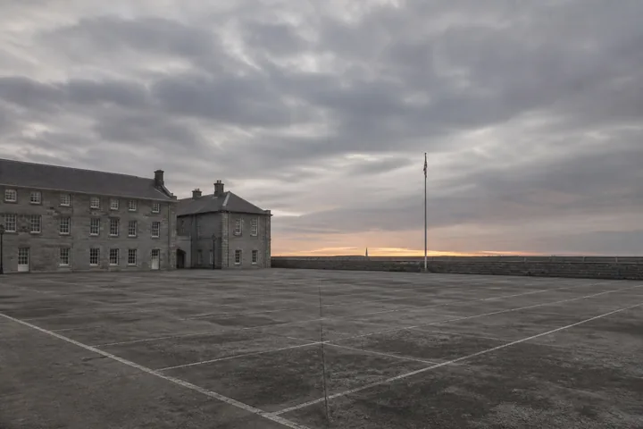 A wide empty drill square at dawn, formation markings faded on the concrete and a single flagpole at the far edge (AI-generated image)