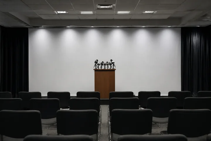 A press-conference room seen from the back: rows of empty chairs facing a lectern with microphones (AI-generated image)