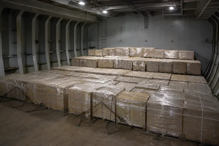 Chained-down cargo pallets stacked in a ship's hold under work lighting (AI-generated image)