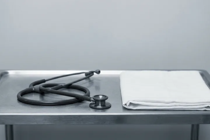 A coiled black stethoscope and a neatly folded white cloth lying on a reflective metal tray under bright, cool light (AI-generated image)