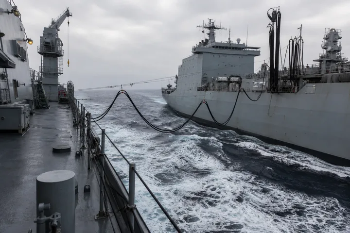 Fuel hoses rigged between two grey hulls under way in moderate swell during a replenishment at sea (AI-generated image)