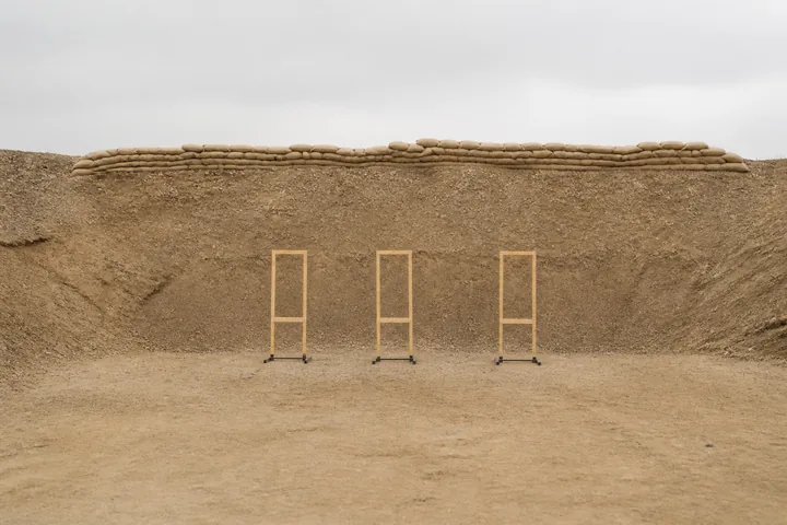 A sandbagged range berm with empty paper target frames standing against it (AI-generated image)