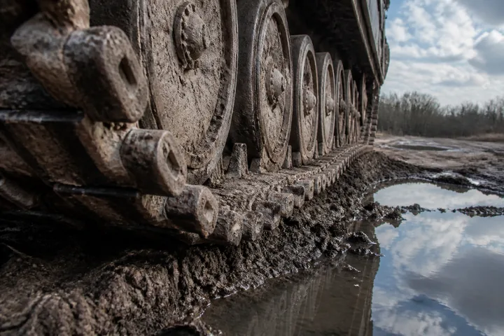 Tank track links and road wheels seen close from ground level, caked with dried mud beside a puddle (AI-generated image)