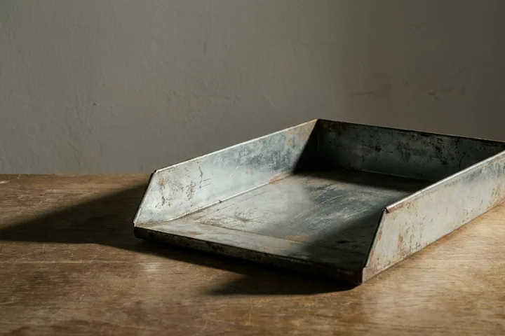An old, rusty rectangular metal tray, open at the front, resting on a wooden surface (AI-generated image)