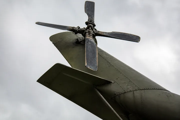 A helicopter's tail rotor and canted stabiliser seen from below against grey sky (AI-generated image)