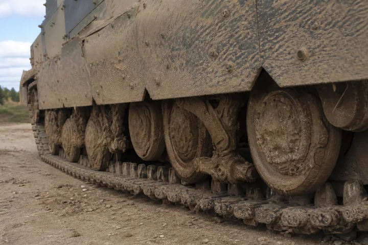 A tracked vehicle's road wheels, torsion arms and skirt plates caked in dried mud (AI-generated image)