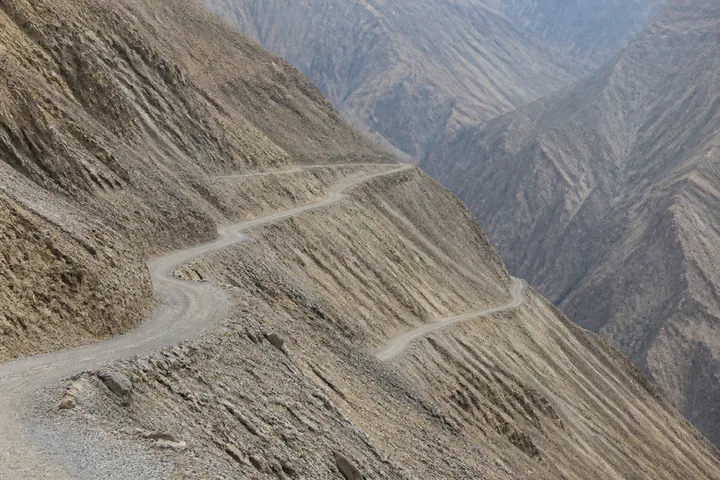A switchback mountain road cut into a scree slope with no barrier on the outer edge (AI-generated image)