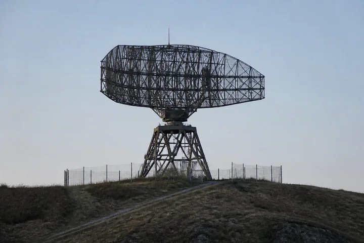 A decommissioned lattice radar antenna on a hilltop against a pale sky (AI-generated image)