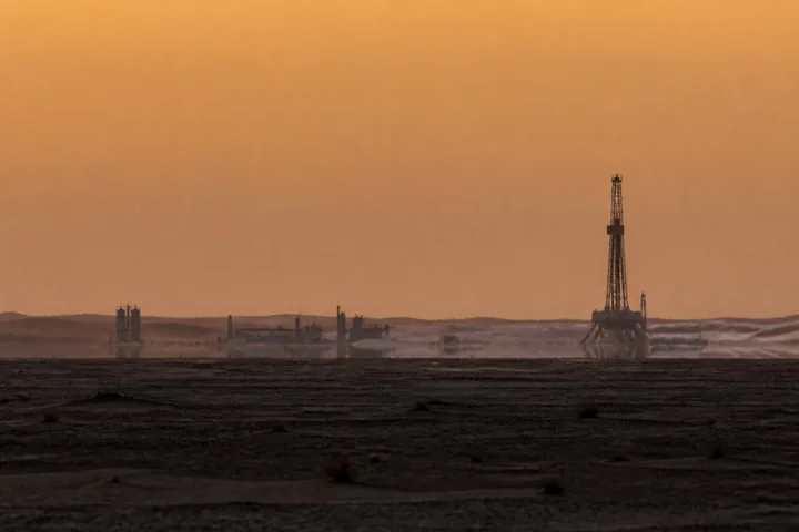 A desert oil installation in silhouette at dusk with heat shimmer above the sand (AI-generated image)