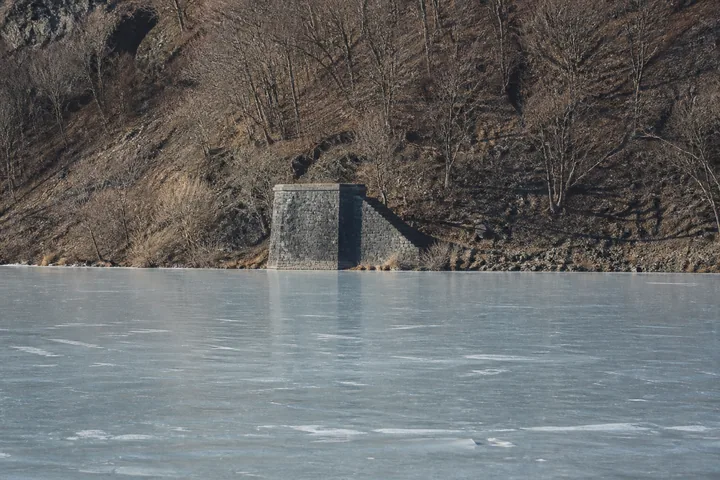 A frozen reservoir with a stone bridge abutment on the far shore and bare hills beyond (AI-generated image)