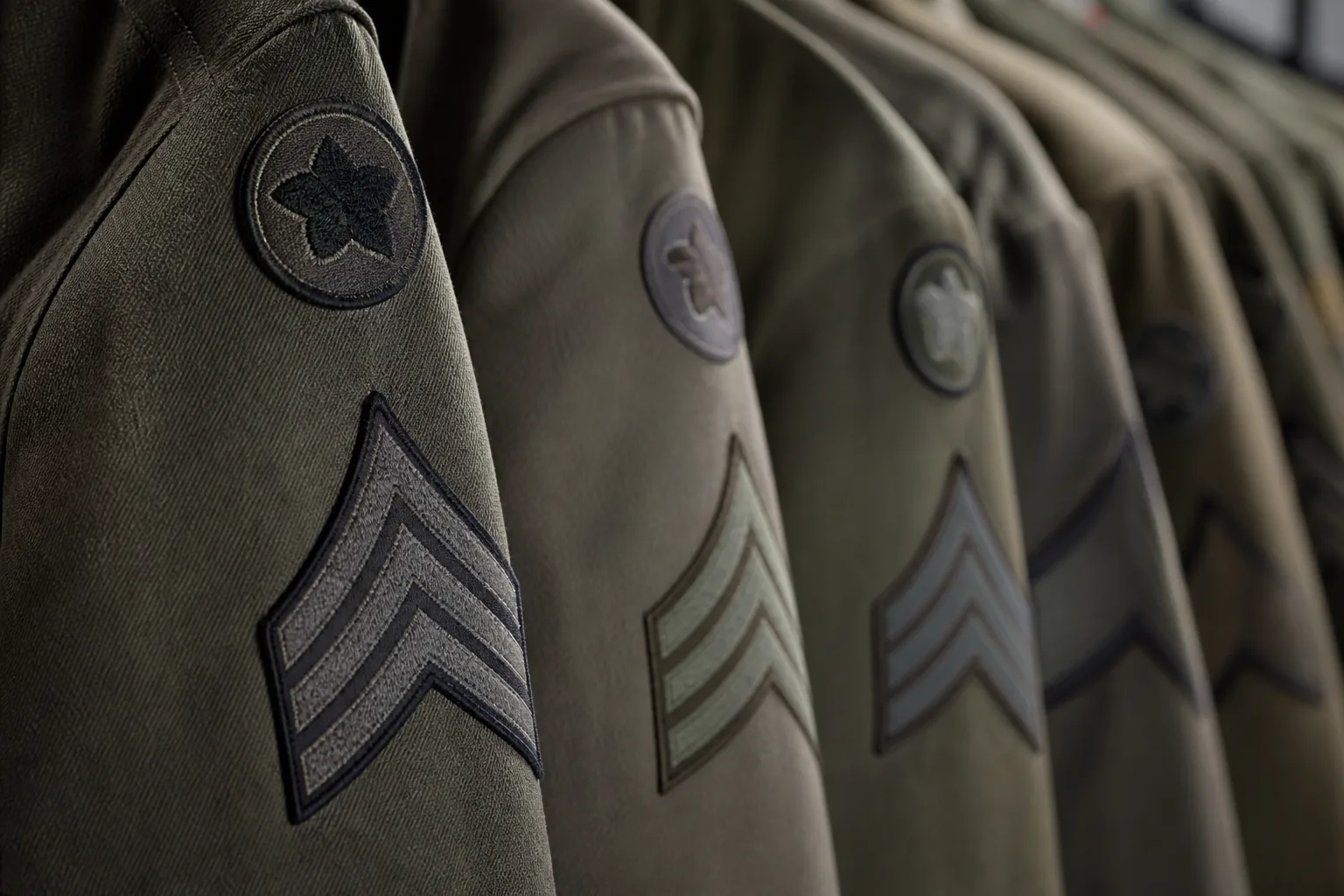 A row of uniform sleeves on a rail, chevrons and rank insignia receding down the line in shallow focus (AI-generated image)