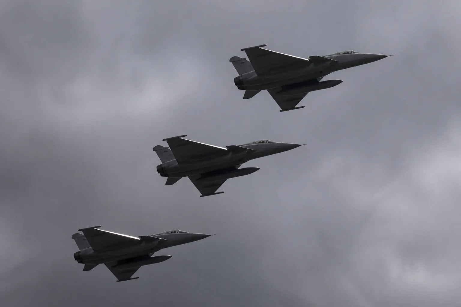Three grey fighter jets in echelon formation seen from below against heavy overcast cloud (AI-generated image)