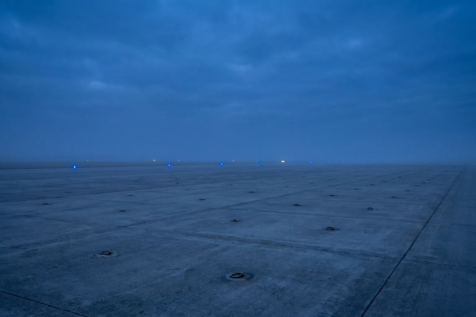 Vast concrete airfield surface with embedded rings under a hazy, cloudy sky (AI-generated image)