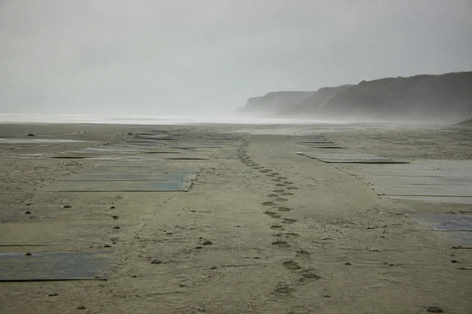 A beach landing zone marked with panels on the sand at low tide, boot prints leading inland (AI-generated image)