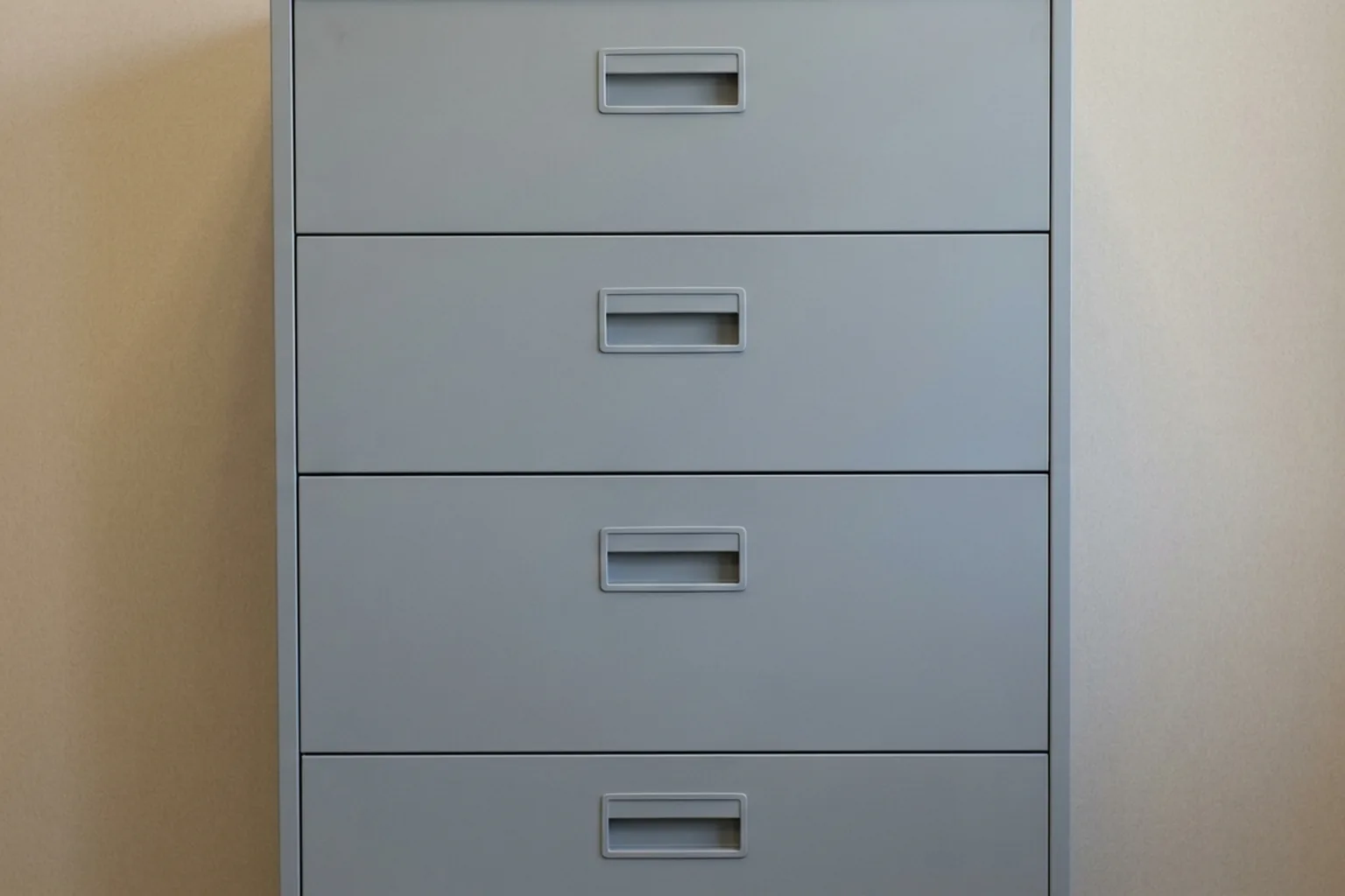A grey four-drawer metal filing cabinet with recessed handles against a textured beige wall (AI-generated image)