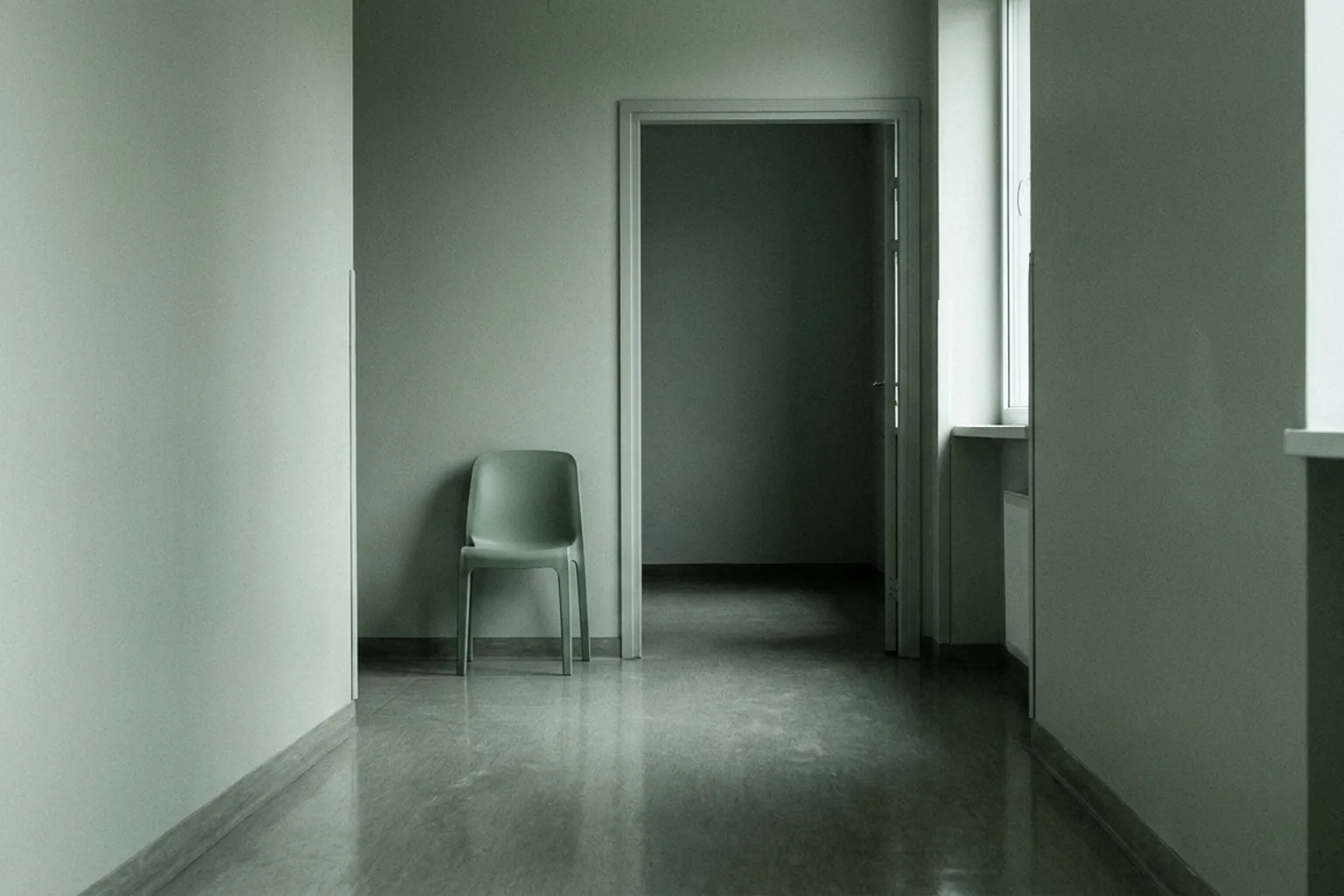 A single light green chair standing against a muted green wall in a corridor with a reflective floor (AI-generated image)