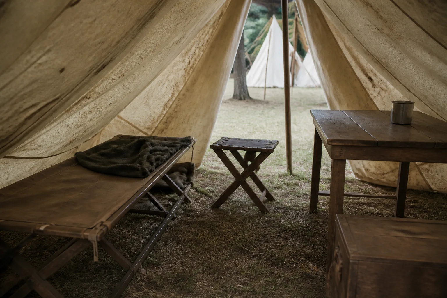 A canvas wall tent interior with a folding cot, a camp stool and a plain table (AI-generated image)