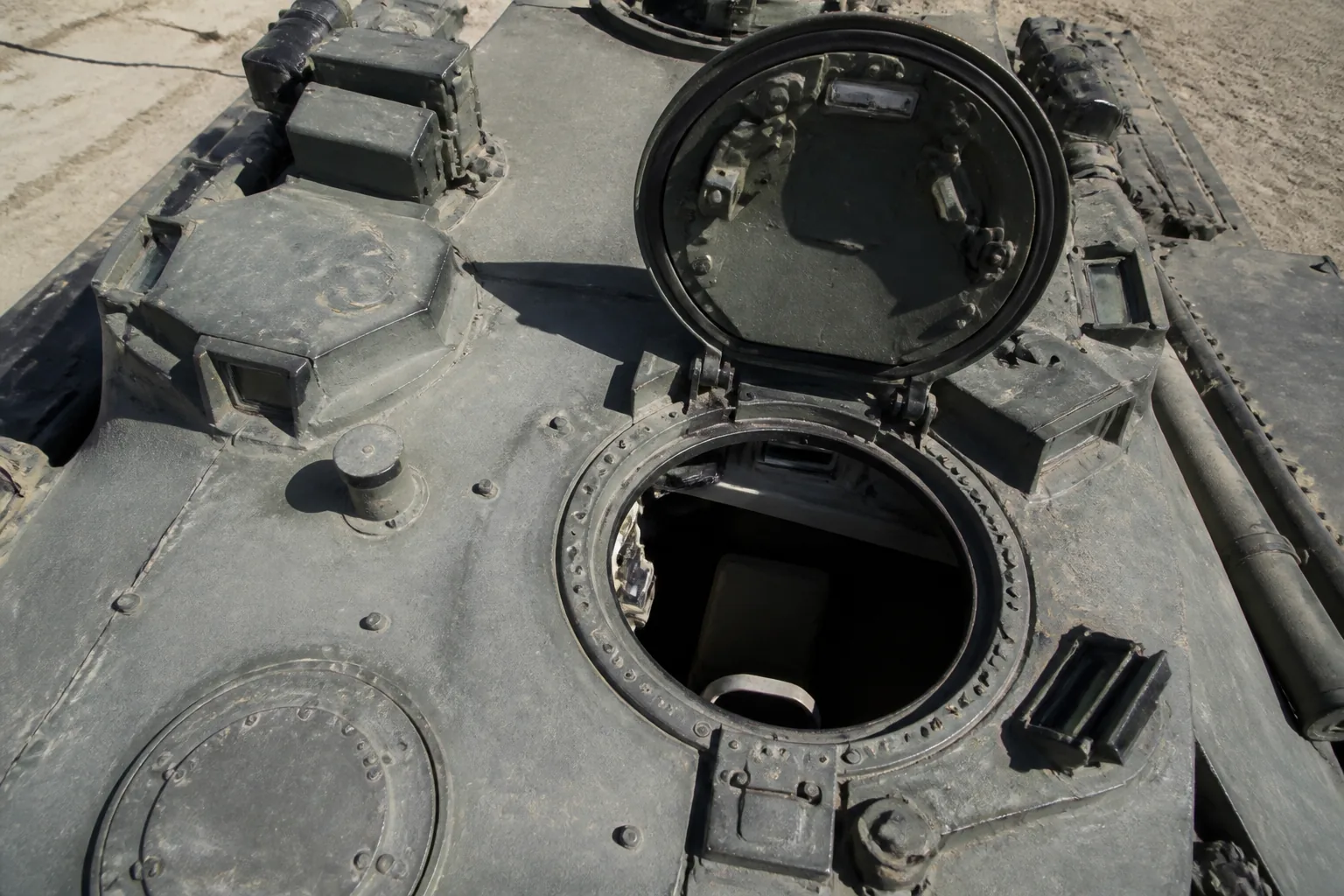 A main battle tank's open commander's hatch and turret roof seen from above, weathered paint and periscopes in detail (AI-generated image)