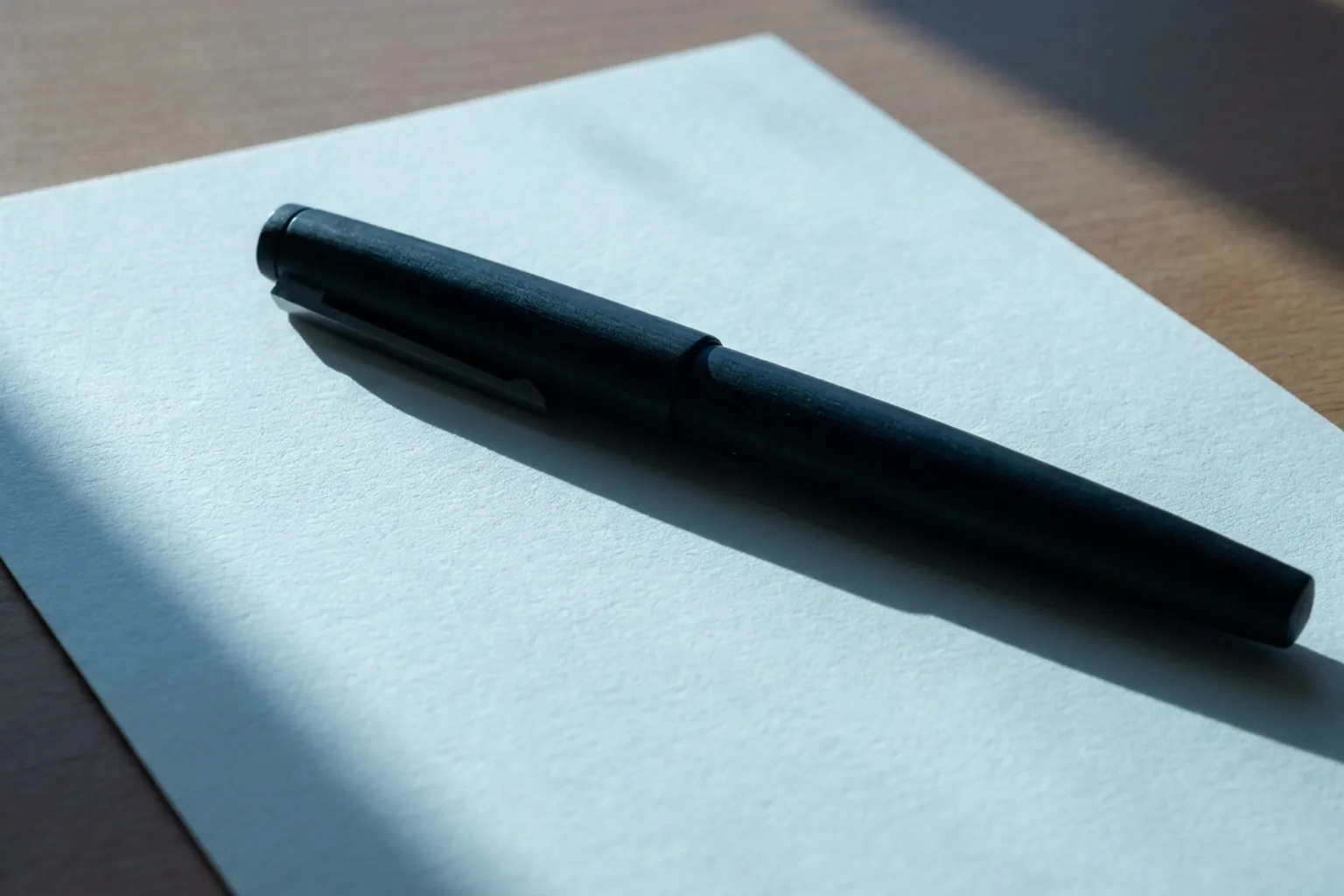 A matte black pen resting on textured white paper on a wooden surface (AI-generated image)