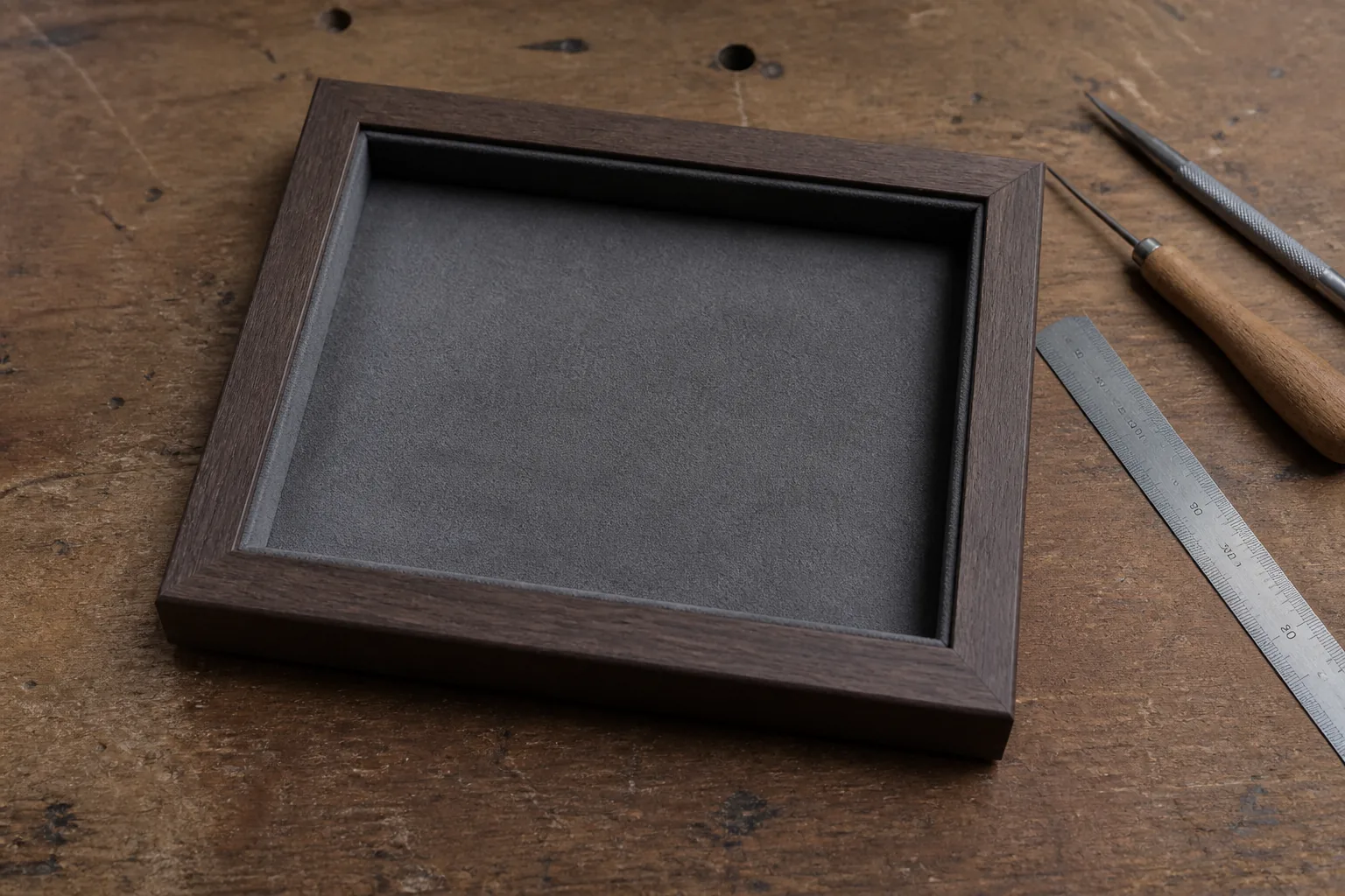 An empty shadow box frame lying face-up on a workbench with tools and a ruler beside it (AI-generated image)