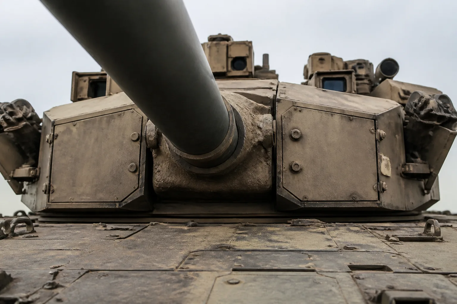 A main battle tank's turret front and gun mantlet seen close from ground level, dust in the joints (AI-generated image)