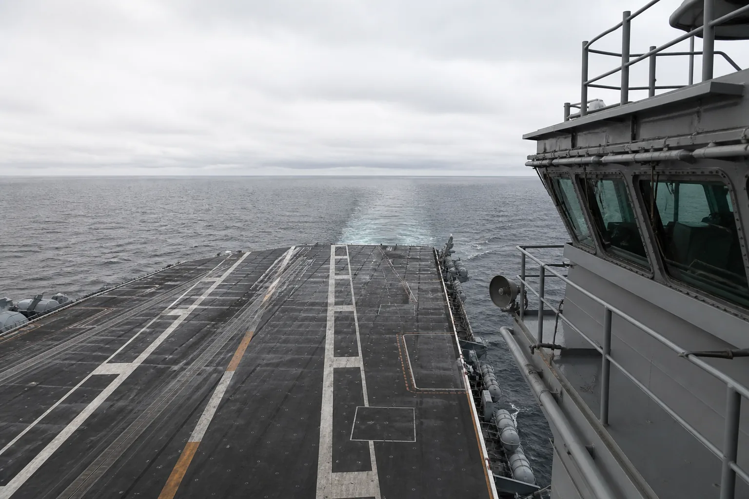 An aircraft carrier flight deck from the island looking aft: catapult tracks, arresting wires, no aircraft (AI-generated image)