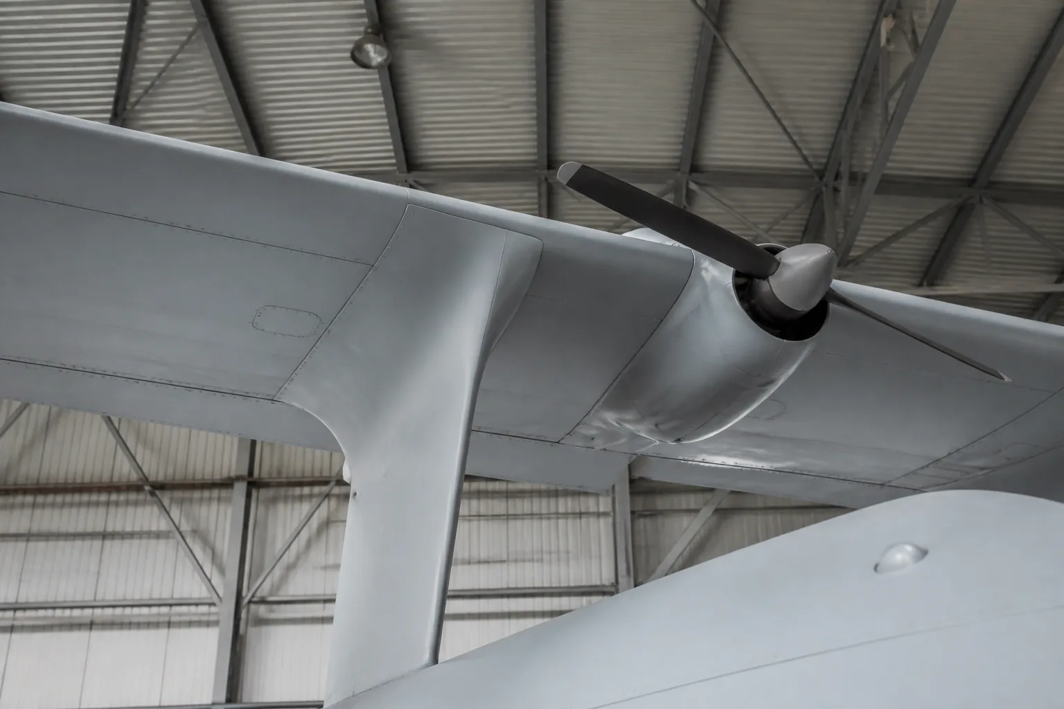 A large unmanned aircraft's high-mounted wing and pusher propeller seen from below in a hangar (AI-generated image)