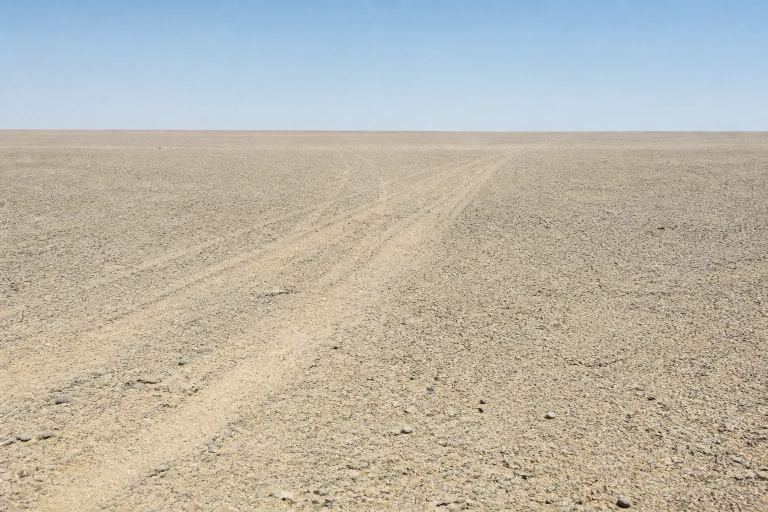Flat gravel desert running to a dead-flat horizon with vehicle tracks crossing it (AI-generated image)